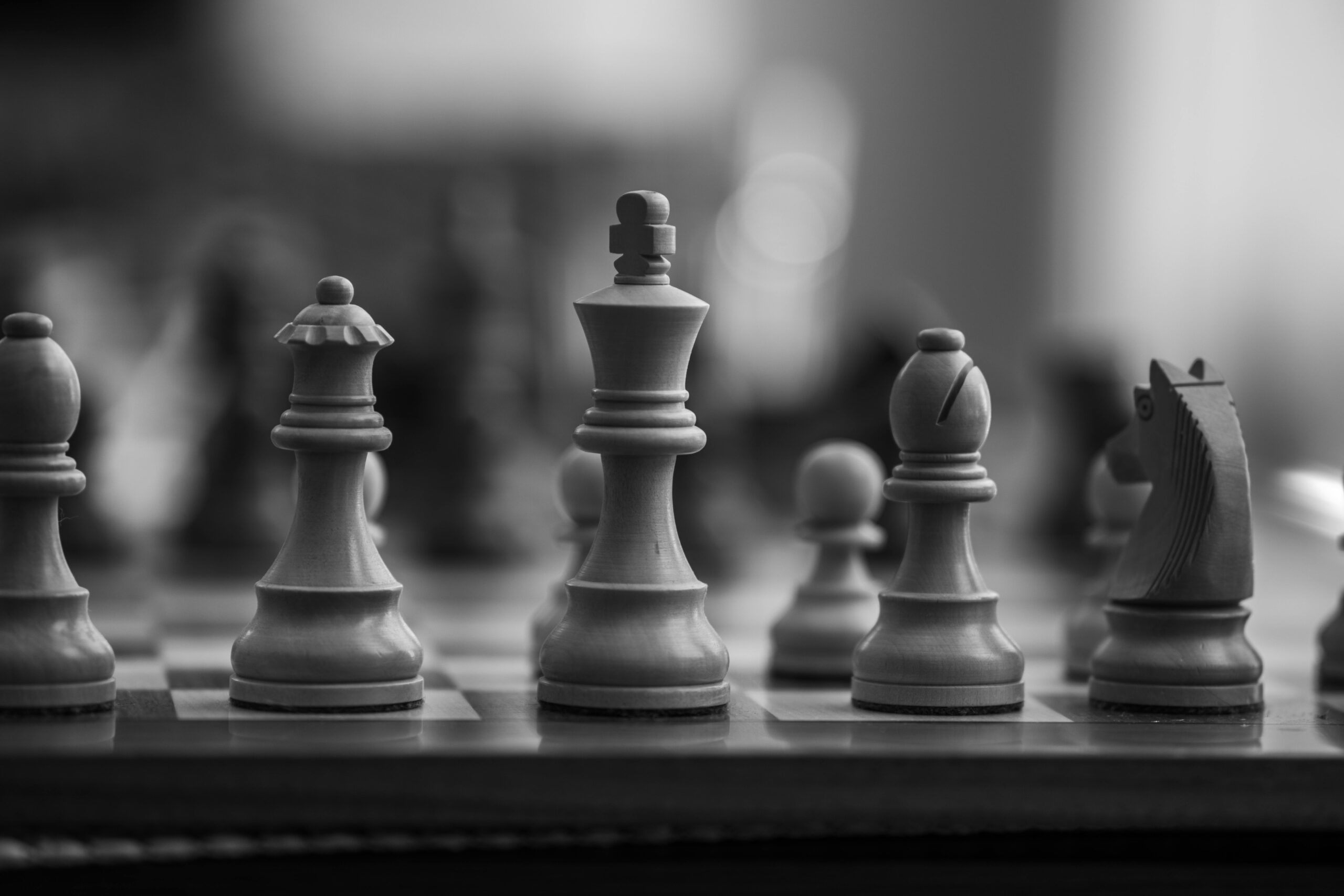 Close-up black-and-white photo of wooden chess pieces mid-game.