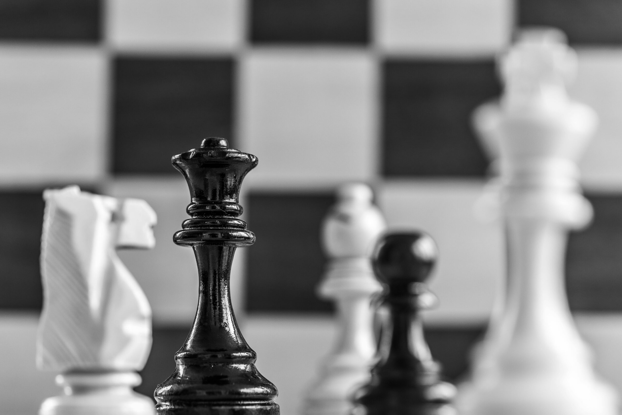 Black queen standing prominently among blurred white chess opponents.